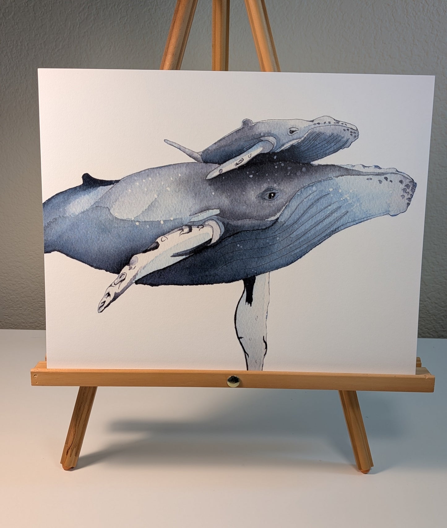 Print of two humpback whales on a white background displayed on a wooden easel.