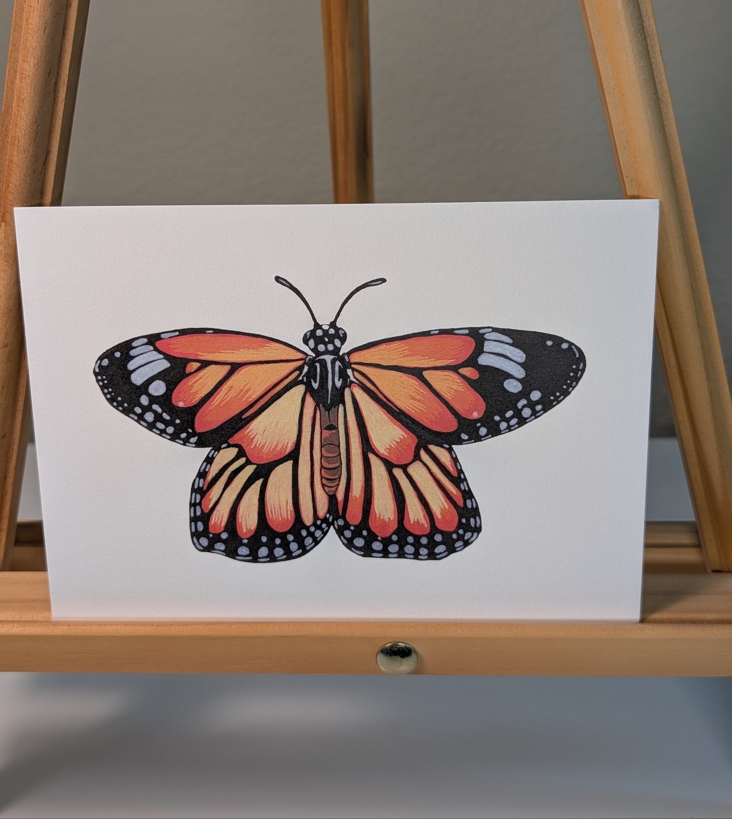 Monarch butterfly illustration on a white background displayed on a wooden easel.