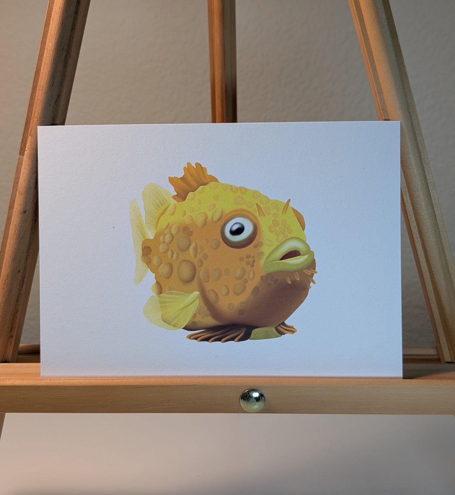 Illustration of a yellow fish on a white card displayed on a wooden easel.